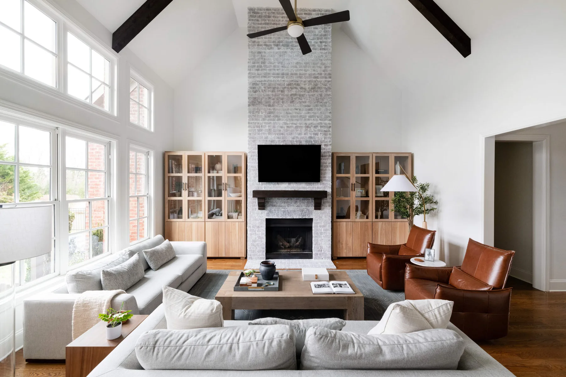 Vaulted great room with white sectionals, leather chairs and a painted brick fireplace, designed by Shelter + Sanctuary